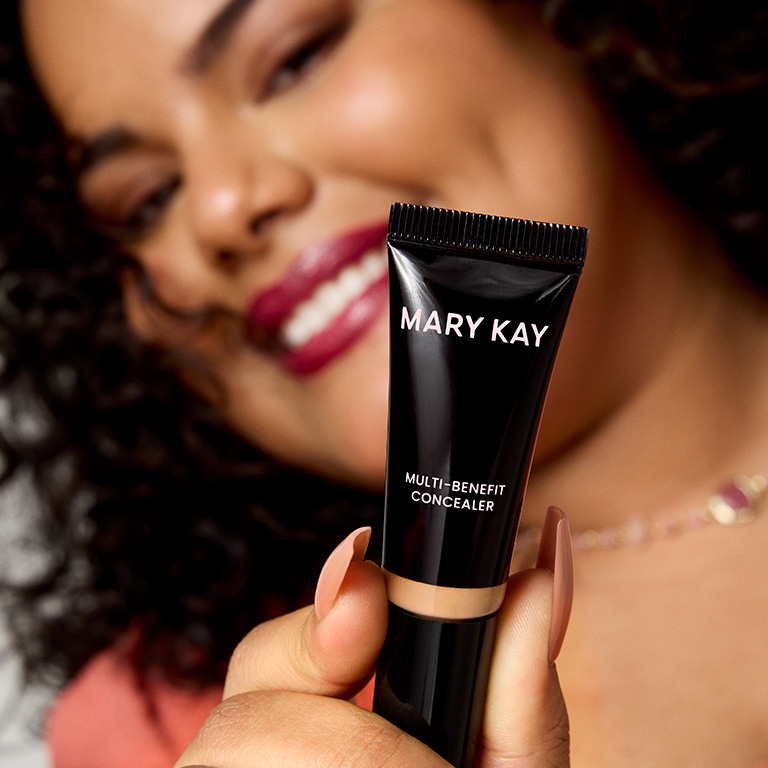 Woman smiling and holding Mary Kay Multi-Benefit Concealer to the camera